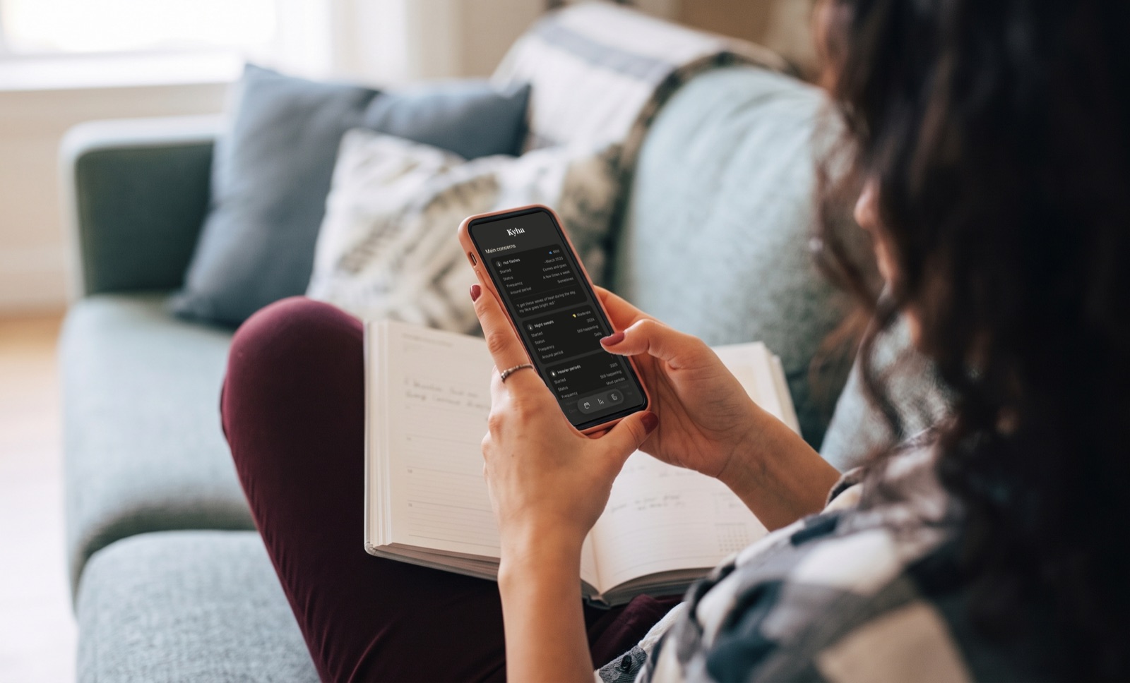 A woman on a couch holding her phone, showing the Main concerns section of her Kyha Health Report